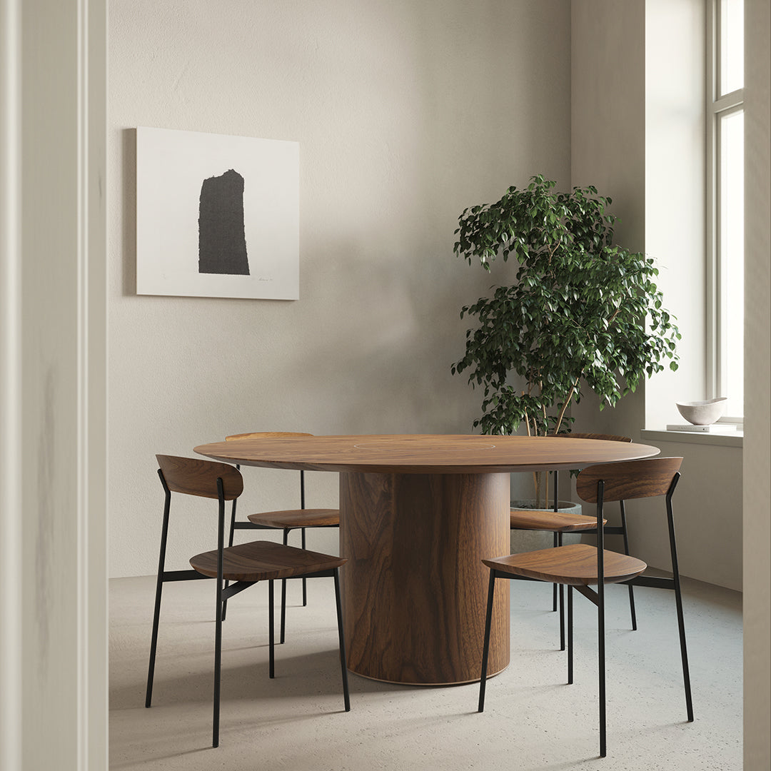 "Round natural wood dining table surrounded by black metal chairs, complementing a neutral-toned, minimalistic interior."