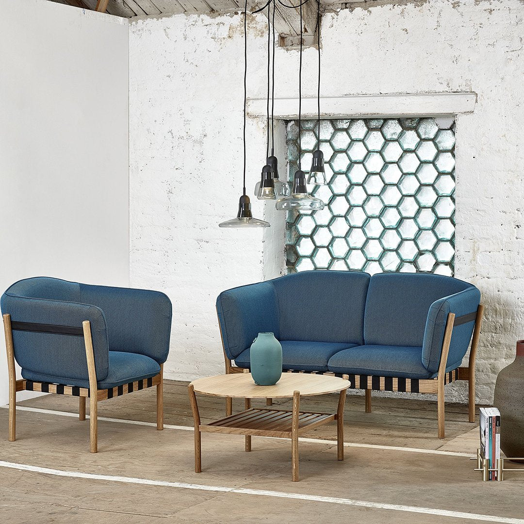 "Two blue upholstered chairs with wooden frames and a light wood coffee table in a bright, minimalist space."