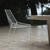 White wire patio chair with sleek, horizontal slat design on a rain-soaked tiled surface. Perfect for outdoor decor.