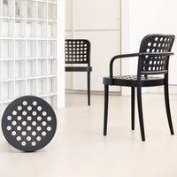Black chair with circular hole pattern and matching round cushion in a minimalist setting. Modern design accents.