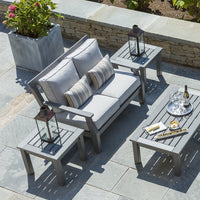 Gray outdoor sofa set with striped cushions, matching gray tables, and lanterns on a stone patio surrounded by greenery.
