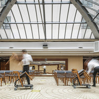 "Stylish wooden chairs against a soft beige background with geometric patterned flooring and a bright skylight."