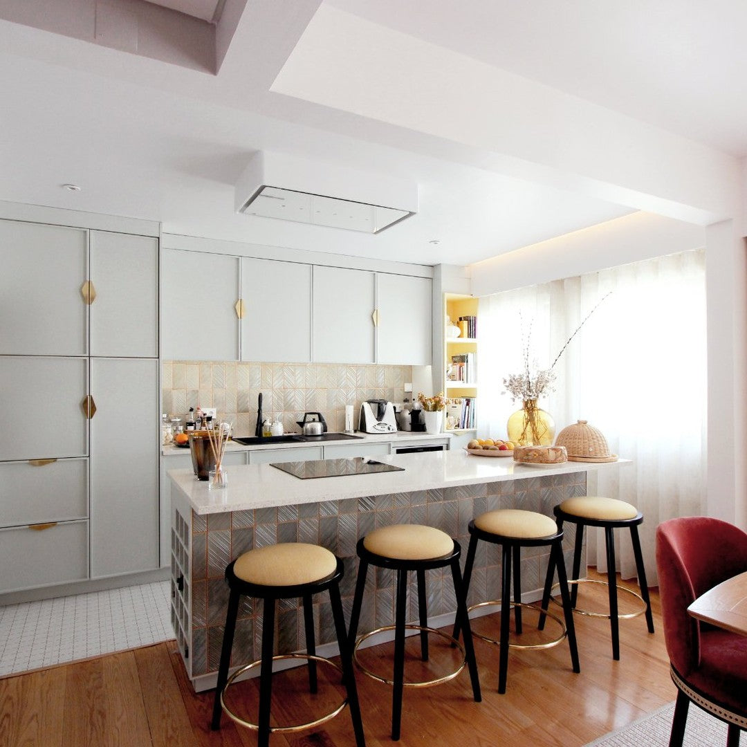 Modern kitchen featuring soft gray cabinets, golden accents, and a patterned tile backsplash. Warm wooden floors complement the design.