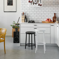 "Black and white bar stools with slatted tops in a modern kitchen featuring gray floors and a white tile backsplash."