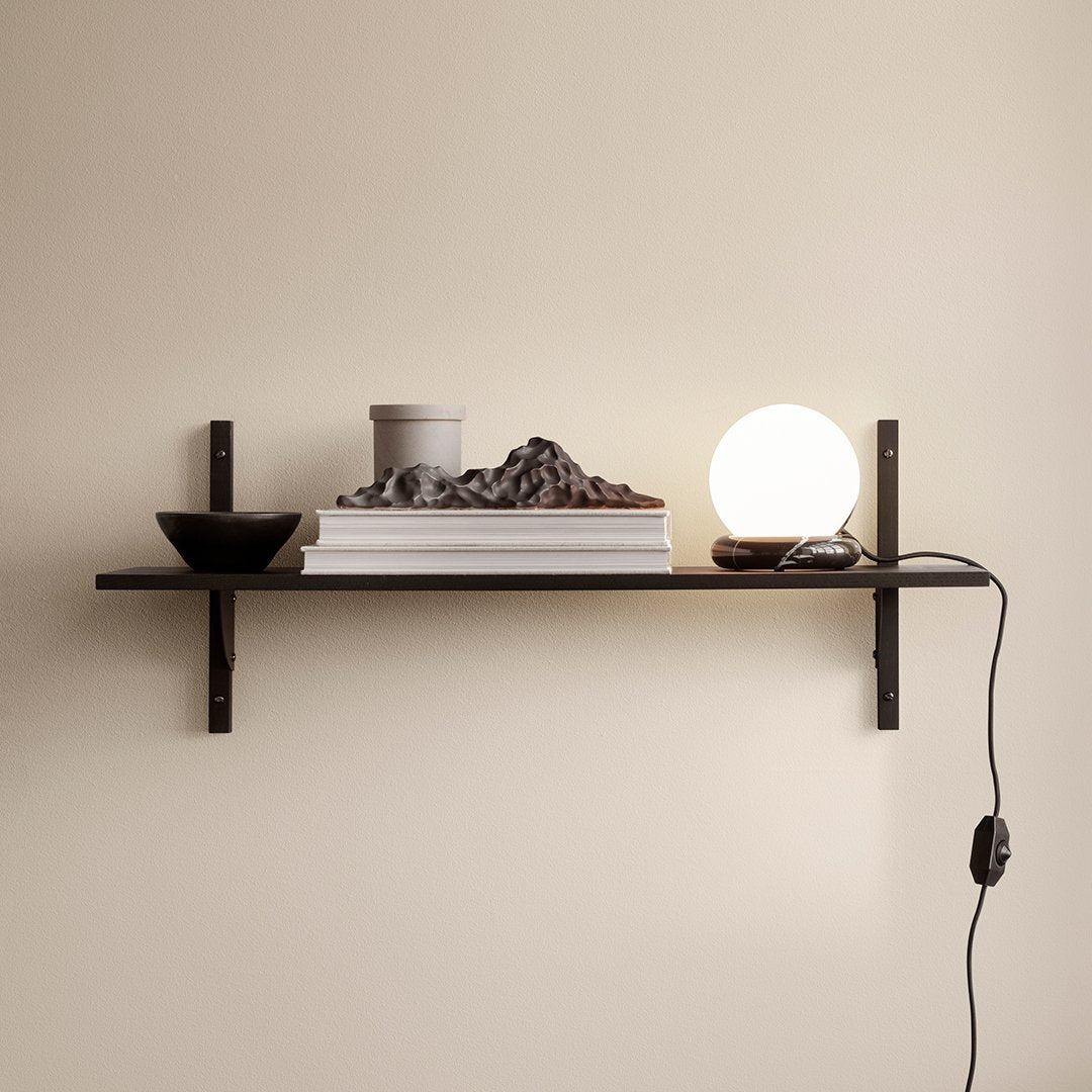 Stylish black shelf with round white lamp, textured black bowl, and gray textured decor on a neutral wall backdrop.