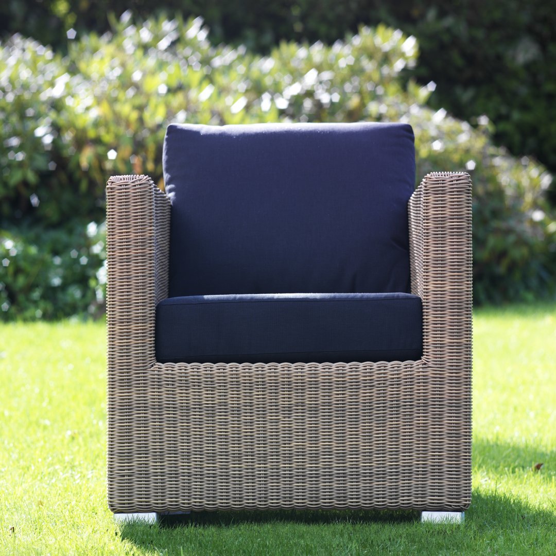 Navy blue cushions on a woven rattan outdoor chair against a vibrant green lawn.