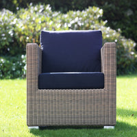 Navy blue cushions on a woven rattan outdoor chair against a vibrant green lawn.