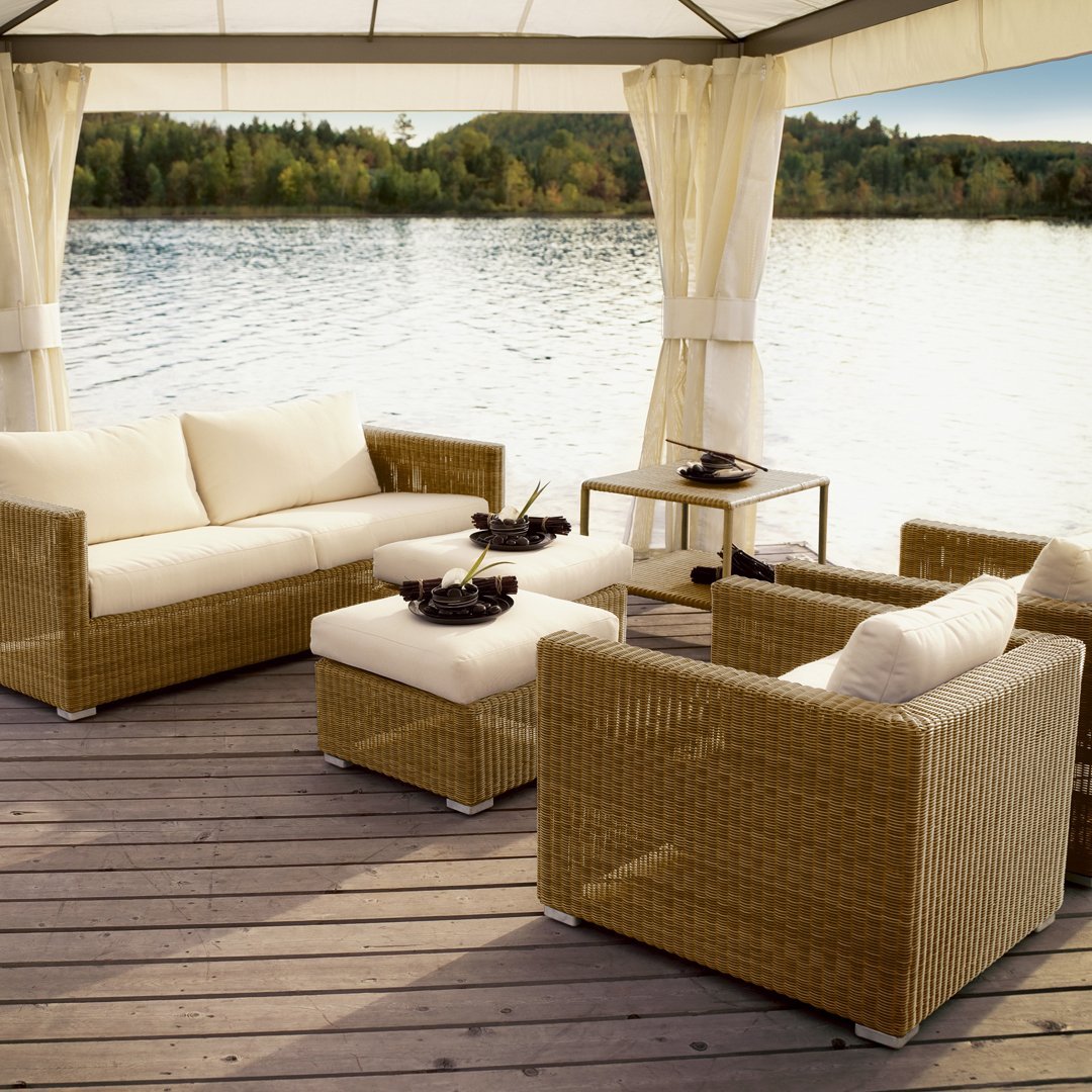 Beige wicker seating set with cream cushions, featuring a simple, elegant design against a serene water backdrop.