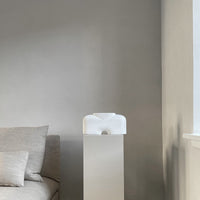White minimalist air purifier with a smooth finish against a light gray wall, adorned with soft beige cushions.