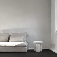 Light gray sofa with subtle texture and design, paired with a white, round accent table on dark flooring.