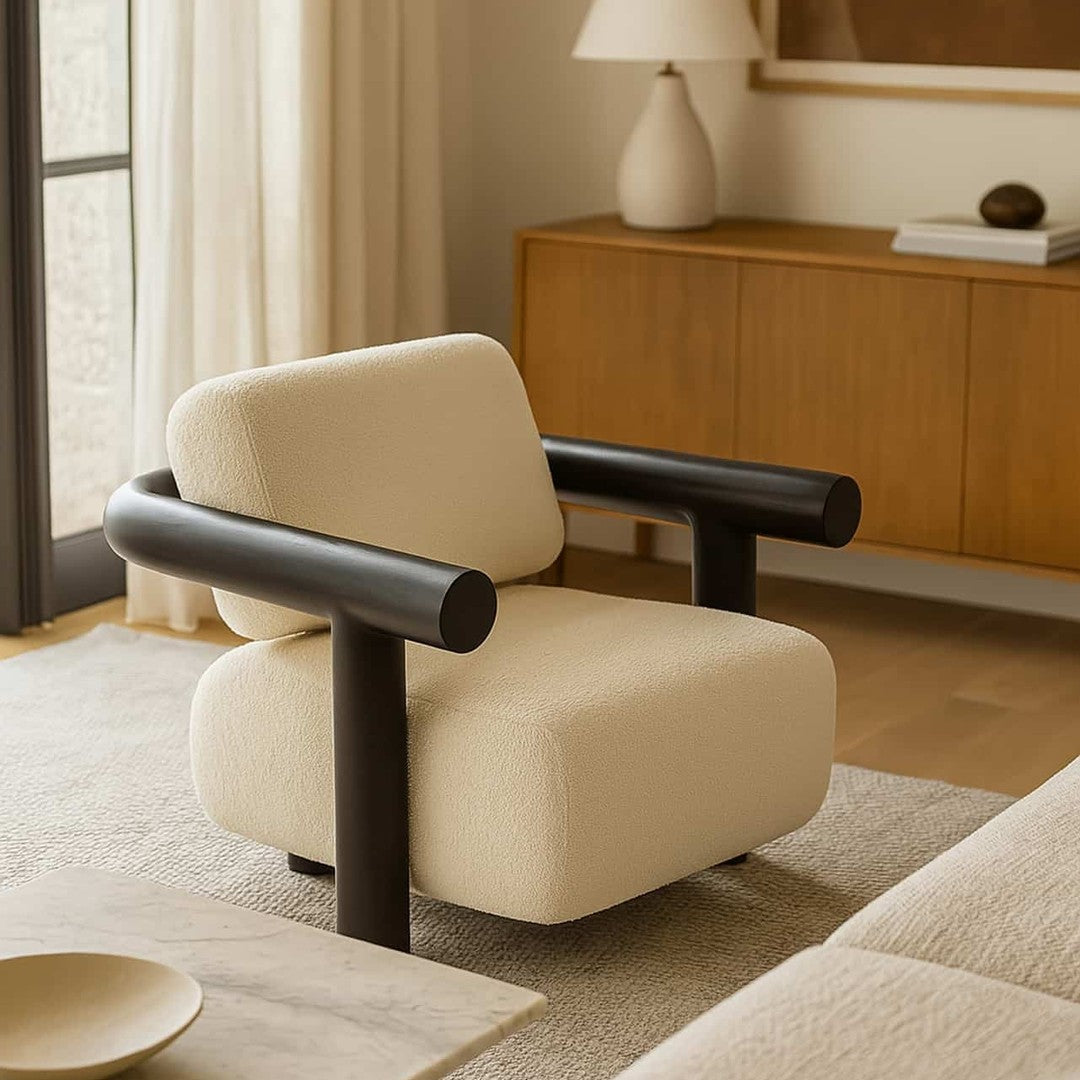 Cream-colored armchair with black rounded armrests, set against a warm, neutral-toned living space.