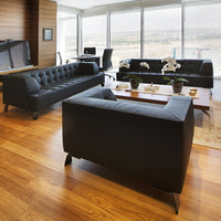 Sleek black leather sofas with tufted design, set against warm wood flooring and a bright, airy backdrop.