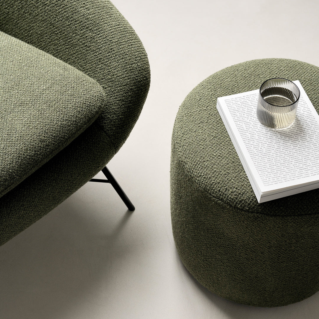 Soft green textured upholstery on a modern sofa, paired with a round green ottoman and a white accent table.