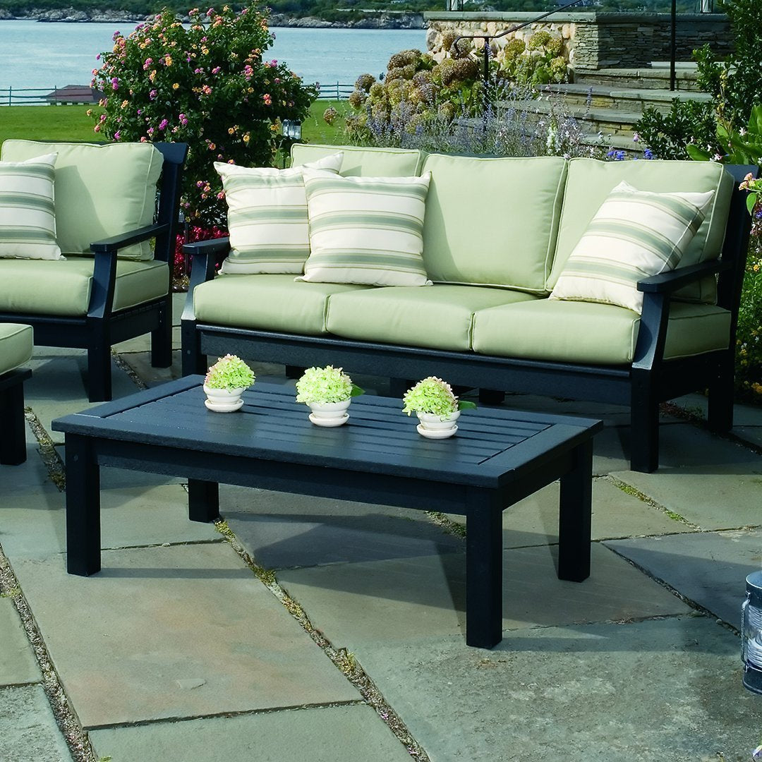 Light green cushions with striped accents on black outdoor furniture set against a stone patio.
