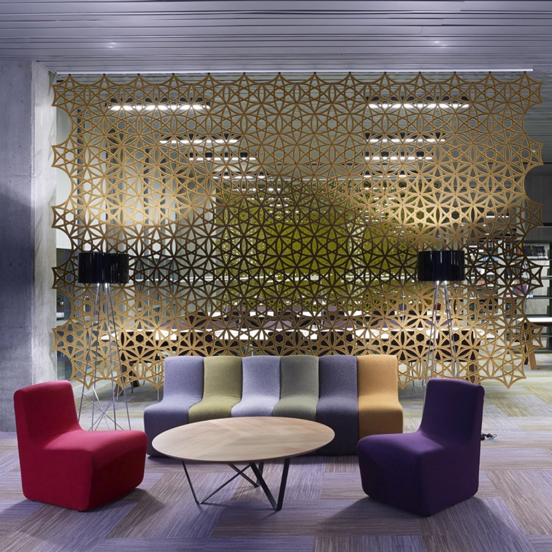 Colorful lounge seating in red, purple, green, and gold geometric-patterned wall backdrop. Modern and stylish design.