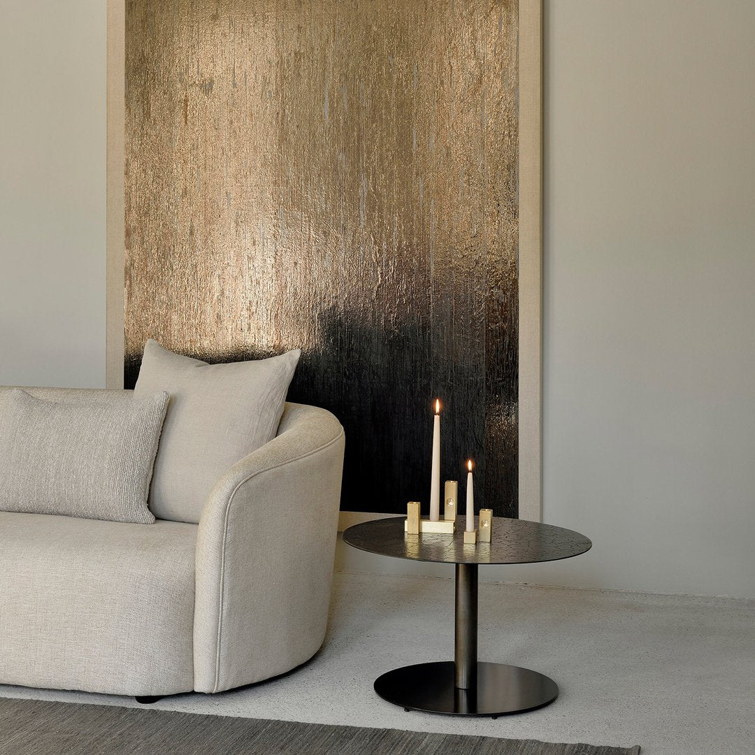 Luxury beige sofa with a sleek black side table and candles, complemented by a shimmering gold and silver wall art backdrop.