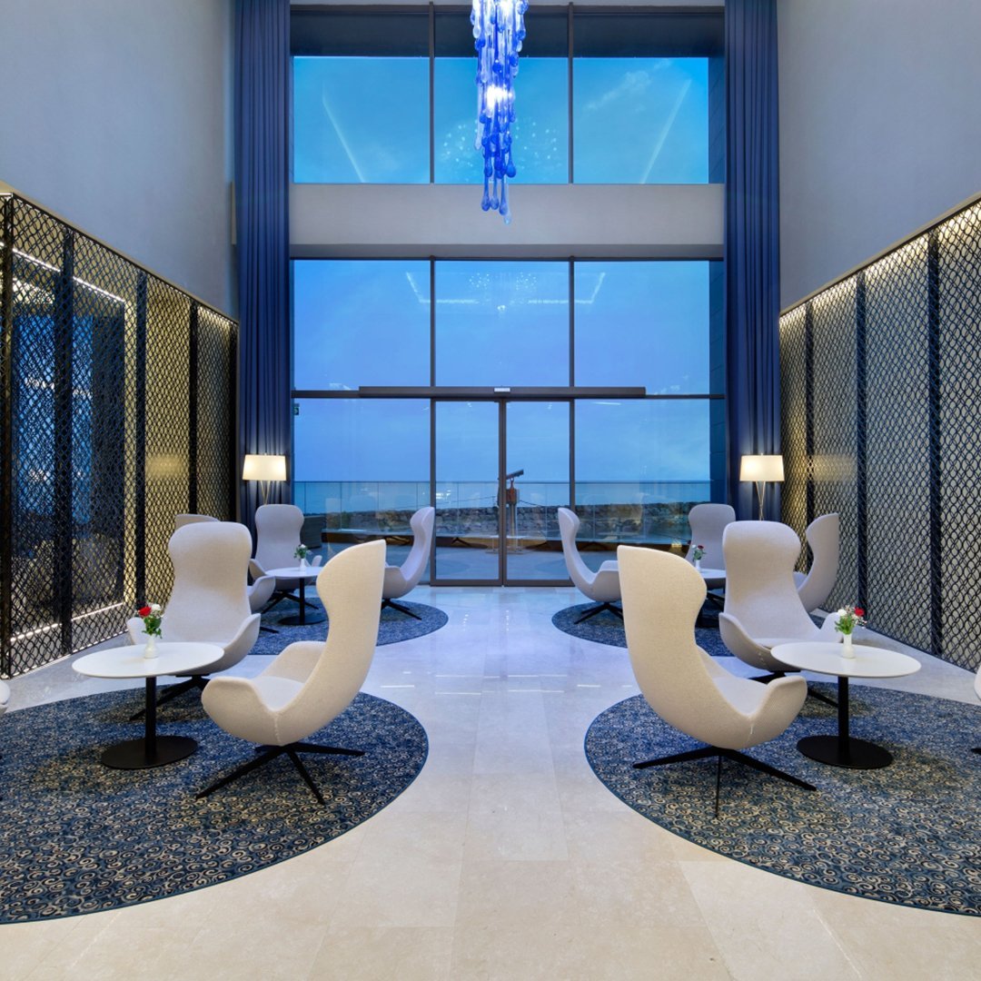 Modern seating in white with circular blue-patterned rugs, set against a sleek, light-filled interior.