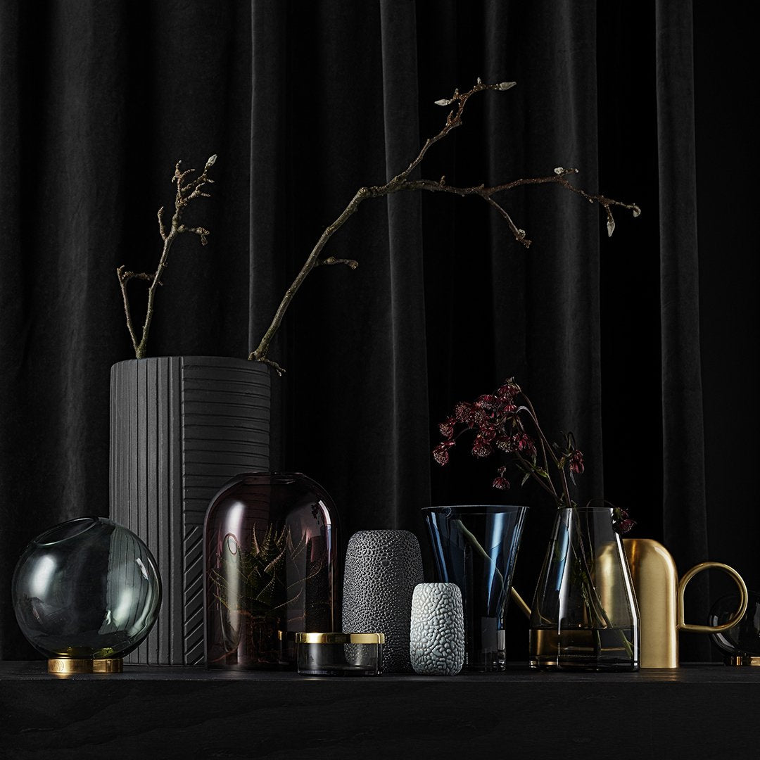 "Collection of colorful vases in various shapes, featuring shades of black, glass, and metallic finishes against a dark backdrop."