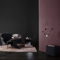 "Modern living space with black accent chair, soft pink and purple wall, and monochrome decor elements."