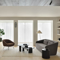 Contemporary living room with neutral tones, brown accents, grey sofa, black tables, and soft white curtains.
