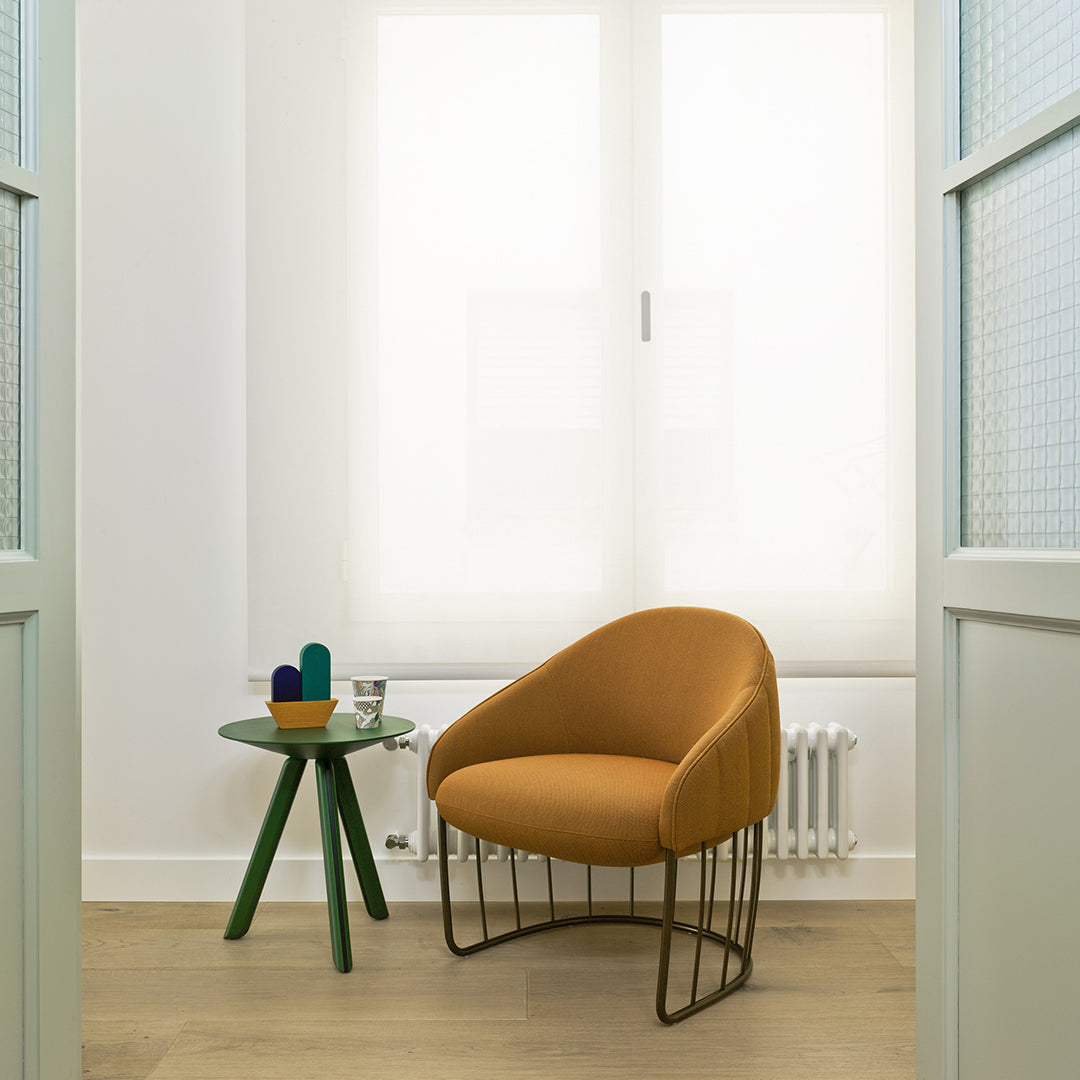 Orange upholstered chair with sleek metal legs, set against light walls and a transparent glass side table.