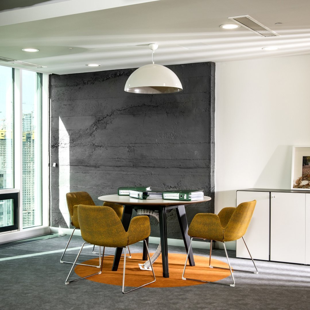 Modern office setting featuring gray walls, orange circular rug, and stylish mustard-yellow chairs around a black table.