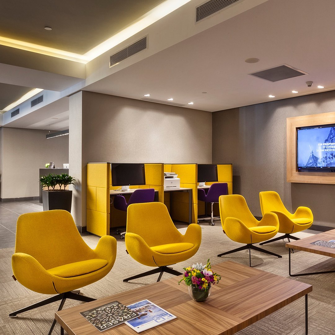 Bright yellow chairs with sleek lines and modern design, set against neutral tones and wooden accents in a stylish lobby.