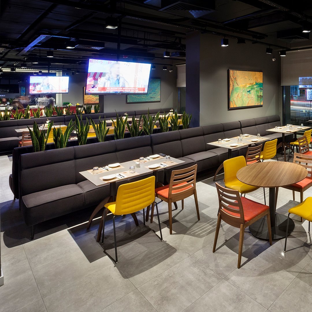 Modern restaurant interior with black seating, vibrant yellow and red chairs, and sleek gray flooring.