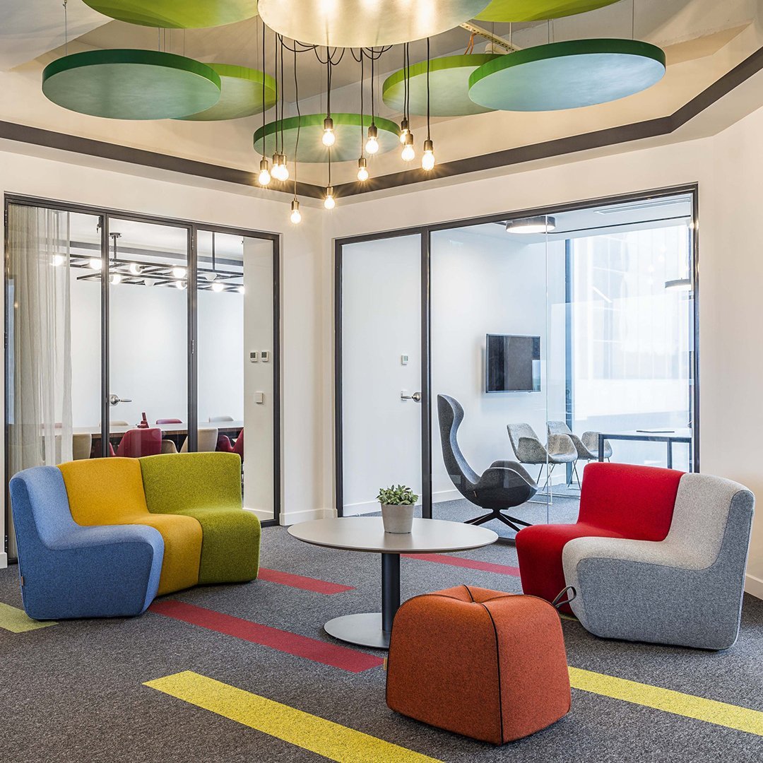 Vibrant armchairs in yellow, green, red, and blue, complemented by a round table and colorful area rug patterns.
