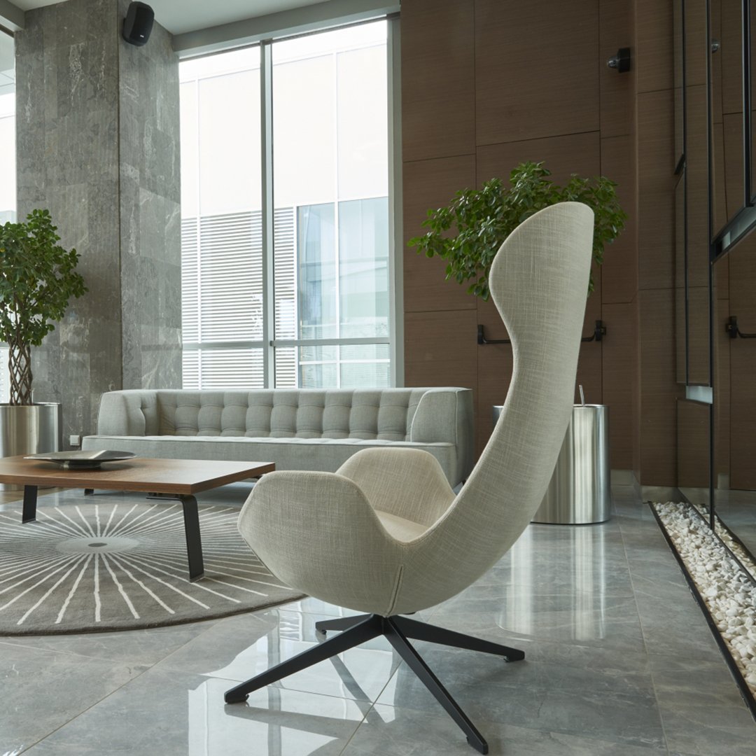 Light beige armchair with a curved silhouette, set against a modern gray and white interior with geometric patterns.