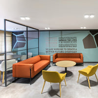 "Modern lounge with orange and yellow sofas, sleek black frames, and a geometric-patterned blue wall."