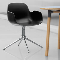 Modern black chair with smooth curves and a chrome base, paired with a light wood table in a minimalist setting.
