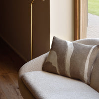 Neutral beige and cream patterned cushion on a light gray sofa in a modern interior setting. Natural light enhances colors.