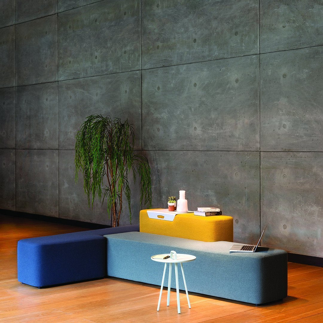 Modern sofa in blue, yellow, and gray tones with a clean, minimalist design against a textured concrete wall.