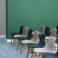 "Row of modern chairs in gray, blue, and teal with wooden legs against a green wall and light blue flooring."