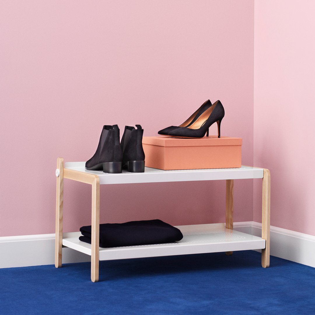 Stylish wooden shoe rack with white shelves, peach storage box, black shoes, on a blue carpet, against a pink wall.