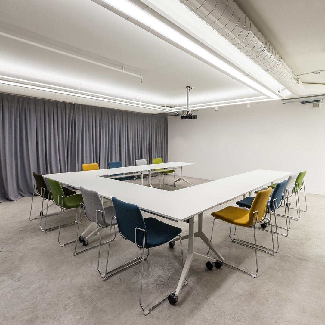 Modern meeting room with gray curtains, white tables, and colorful chairs in blue, green, yellow, and orange.