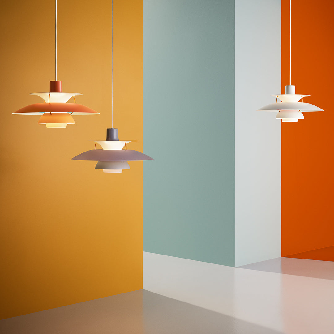 Colorful pendant lights against a backdrop of orange, soft blue, and white geometric walls. Modern design and elegance.