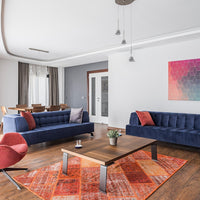 Vibrant orange and red patterned rug with a geometric design, contrasting against blue sofas and neutral walls.