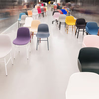 Colorful collection of modern chairs in various patterns: pink, blue, yellow, purple, and black, arranged in a bright space.