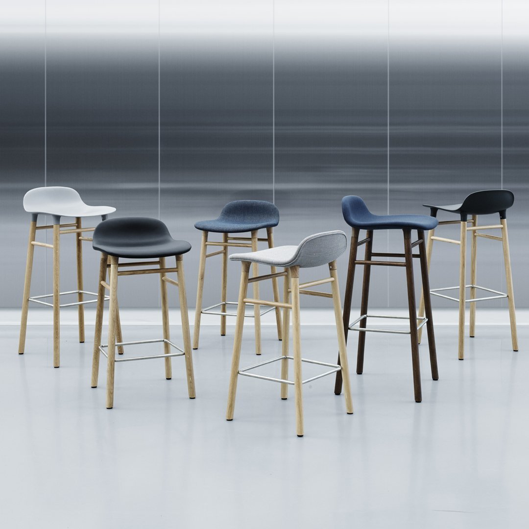 Set of modern bar stools in black, white, and grey with wooden legs against a sleek gray backdrop.