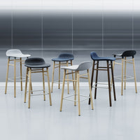 Set of modern bar stools in black, white, and grey with wooden legs against a sleek gray backdrop.