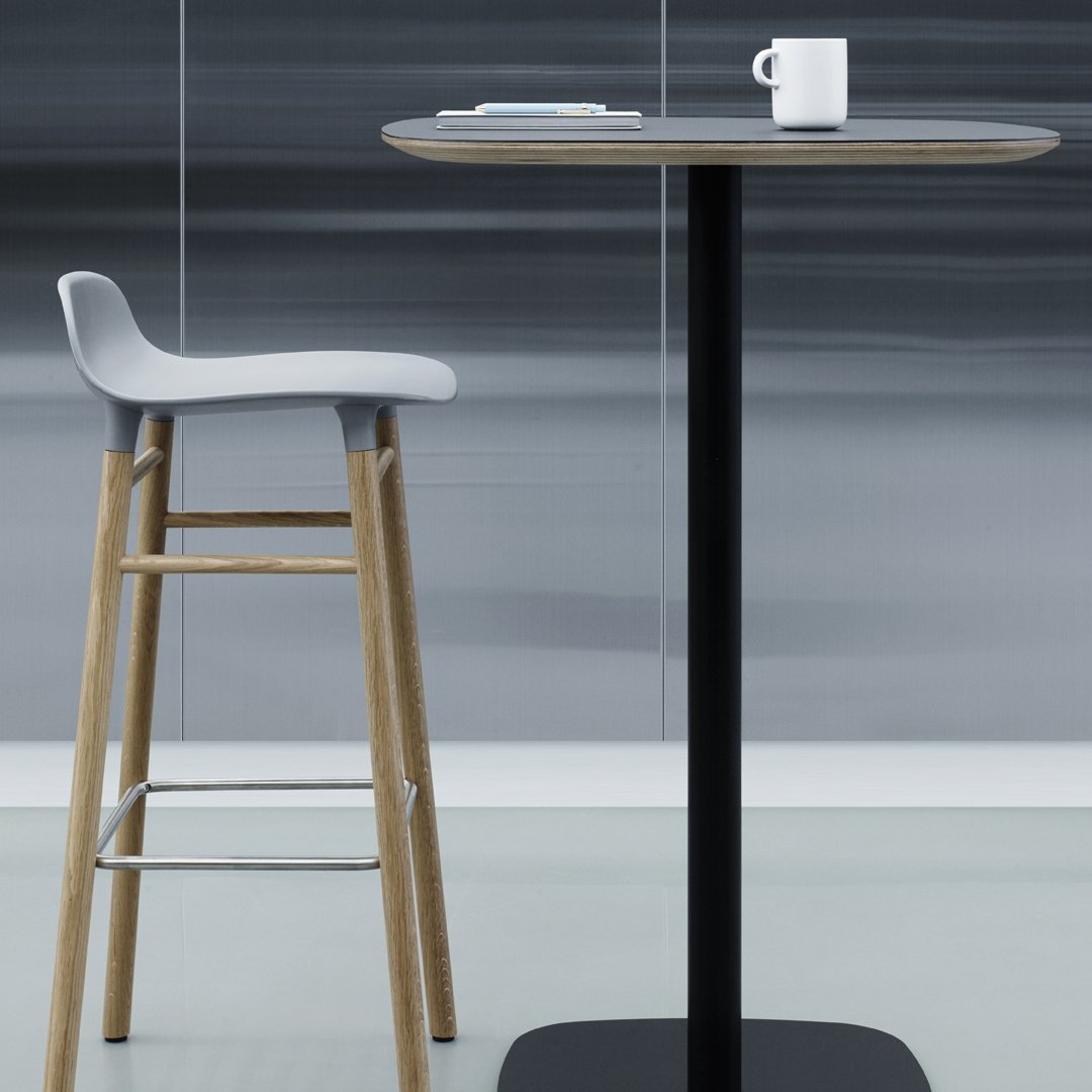 Modern bar table with a black base, round grey top, and a light wood stool featuring a soft grey seat.