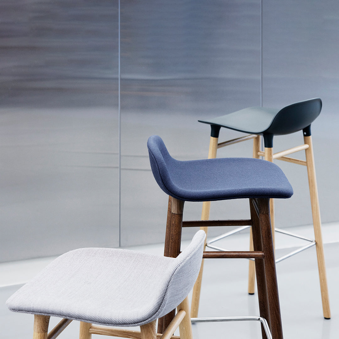 "Modern bar stools in gray, navy, and green upholstery with wooden legs against a sleek, metallic background."