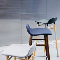 "Modern bar stools in gray, navy, and green upholstery with wooden legs against a sleek, metallic background."