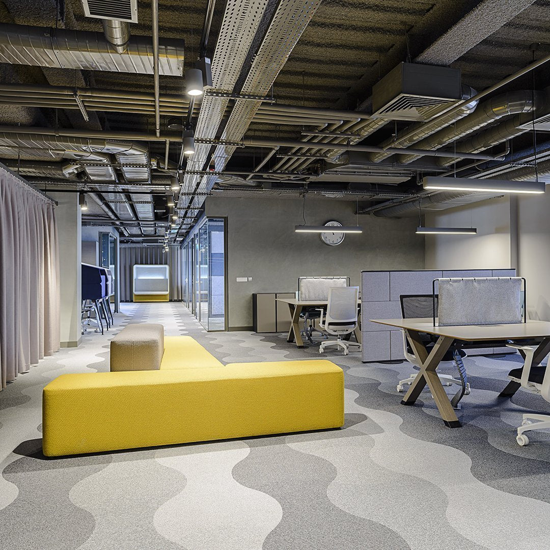 Modern office interior featuring a yellow sofa and wavy gray carpet pattern in a contemporary workspace design.