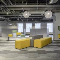 Modern office space featuring yellow, green, and gray seating with wavy patterned flooring and bright lighting.