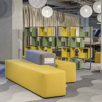 Yellow and gray tubular sofa alongside green and yellow shelving units in a modern, patterned workspace.
