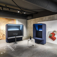 Modern seating pods in deep blue with sleek lines, complemented by a minimalist white table and subtle concrete backdrop.