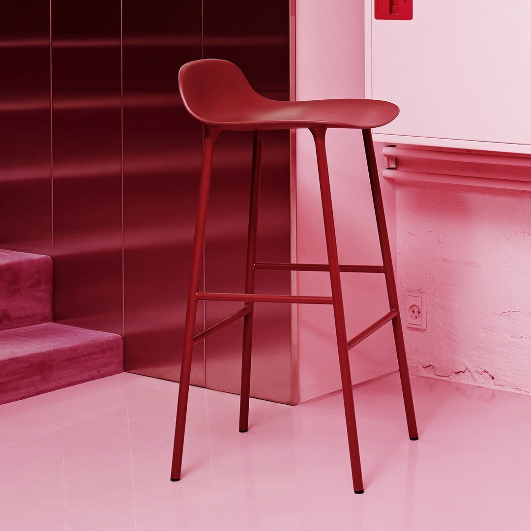Red modern bar stool with a sleek design, featuring a smooth surface and minimalist style against a pink backdrop.